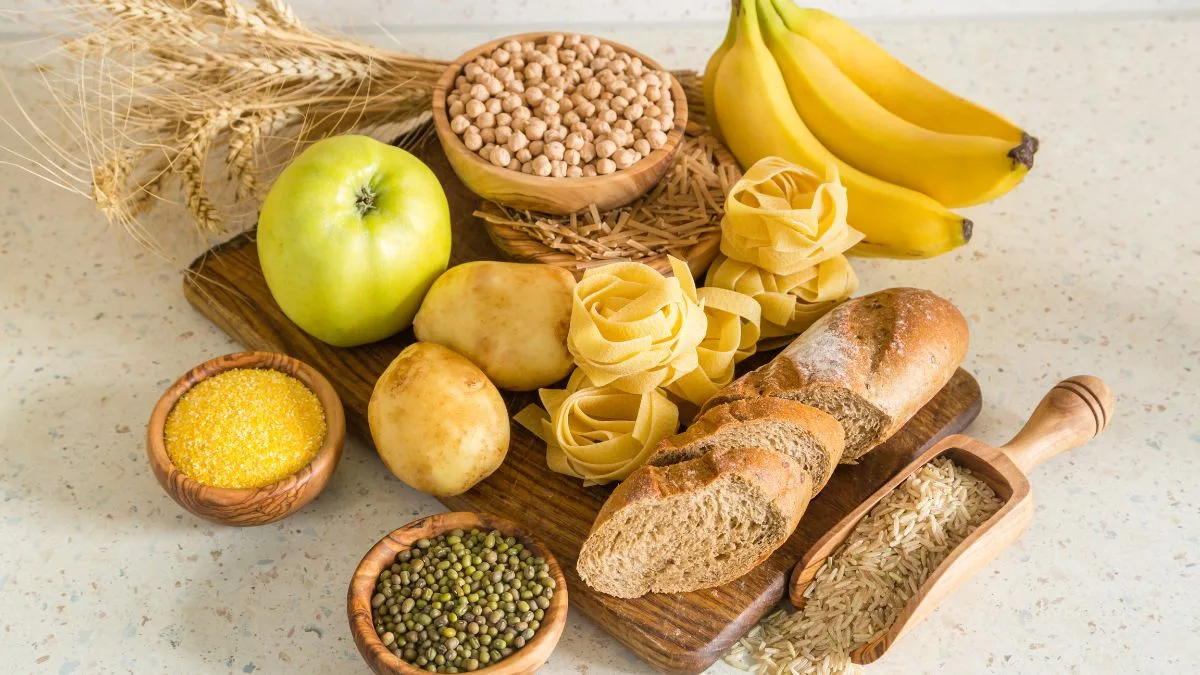 Light surface with bananas, apple, wheat stalks, and wooden bowls containing various grains and pasta
