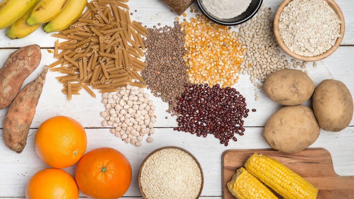 White wooden surface with organized rows of different carbohydrate sources including pasta, beans and fruits