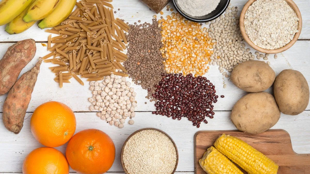 White wooden surface with organized rows of different carbohydrate sources including pasta, beans and fruits