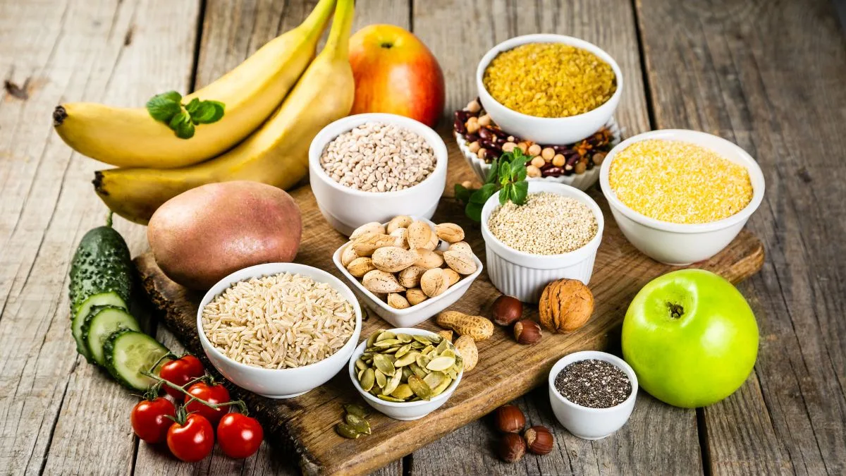 Wooden board with bananas, apple, various grains in bowls, nuts and seeds arranged neatly