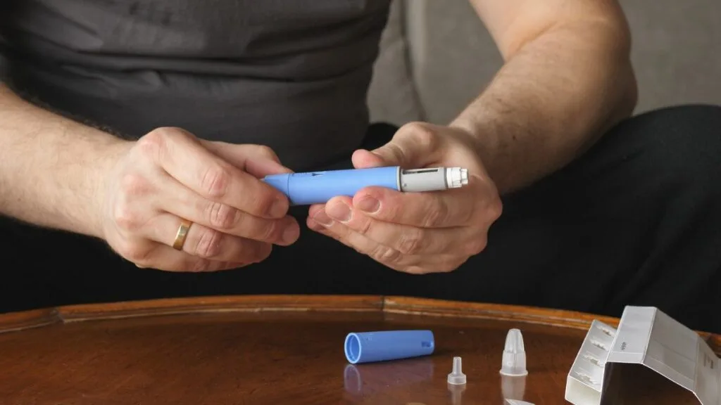 Person holding Ozempic injection pen device with supplies on wooden table for diabetes treatment