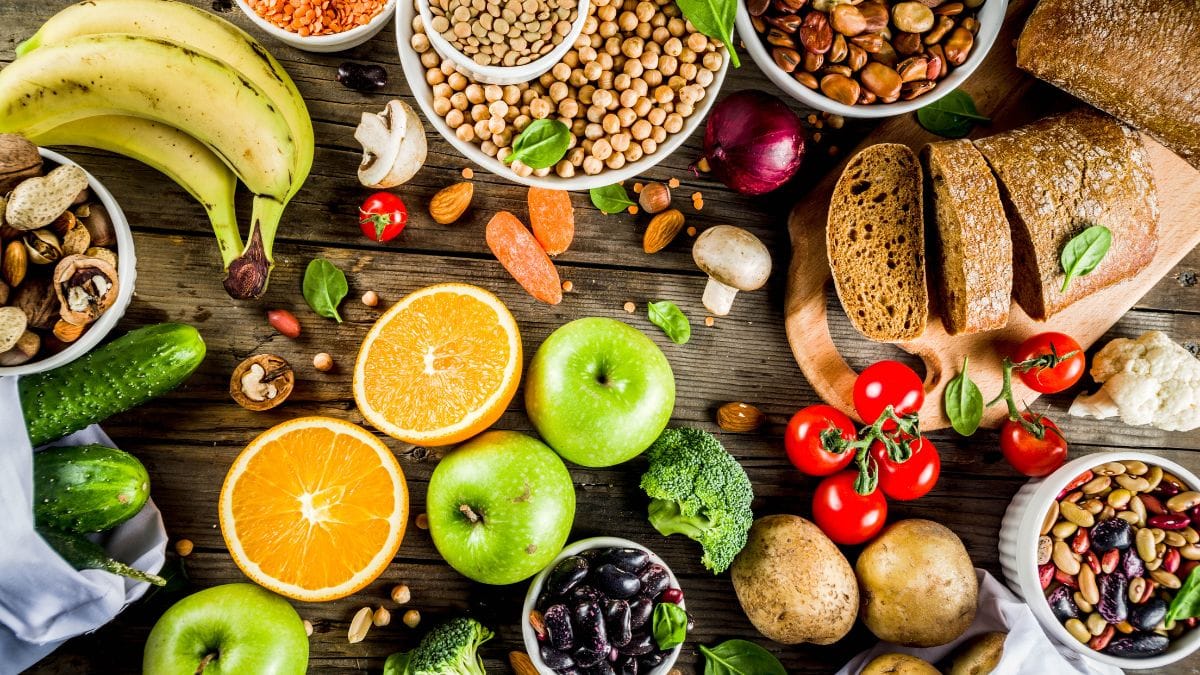 Dark wooden table with colorful array of plant proteins including beans, nuts, fruits and vegetables
