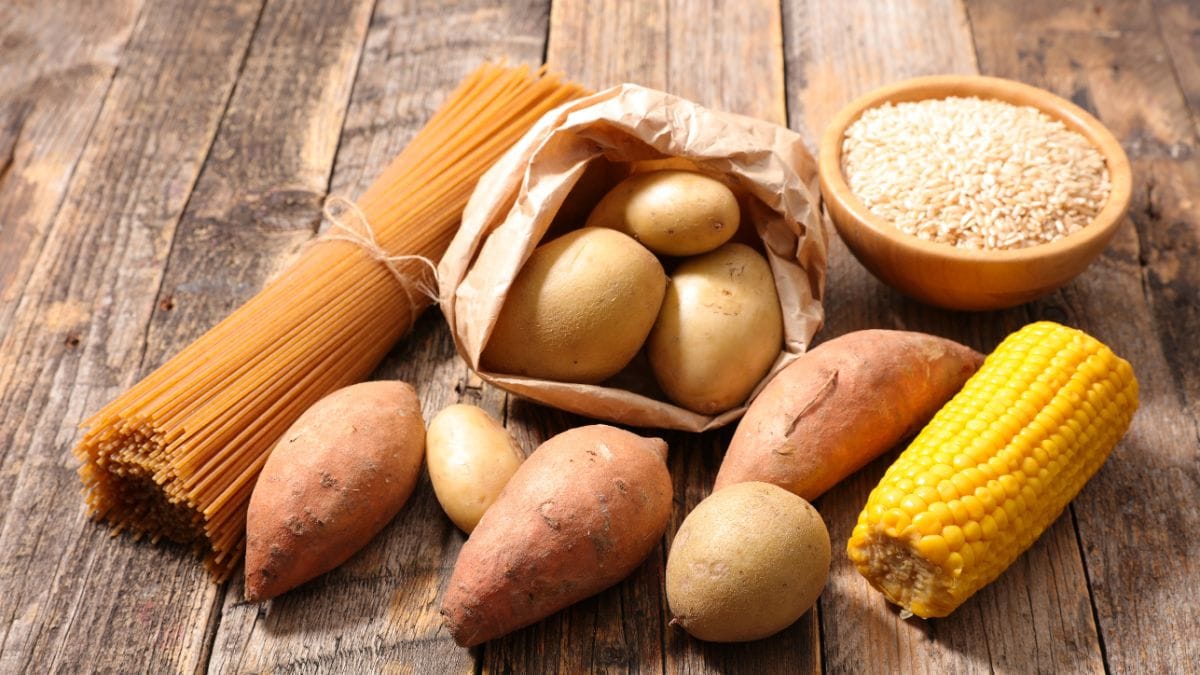 Wooden planks with potatoes, corn cob, pasta bundle, and bowl of quinoa grains
