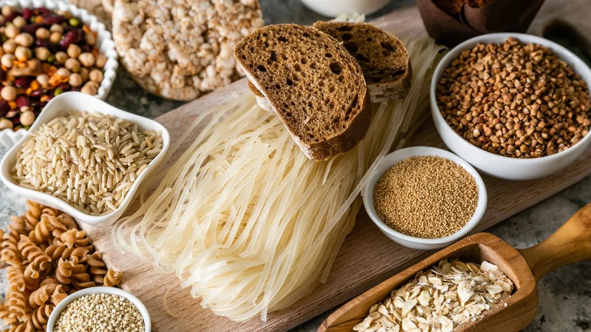 Wooden cutting board with sliced whole grain bread, pasta, and bowls of various grains and legumes